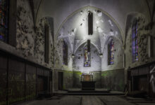 Kapellenchor mit weißer Gewölbeapsis, abblätterndem Putz und Buntglas am Altar im Lost Place